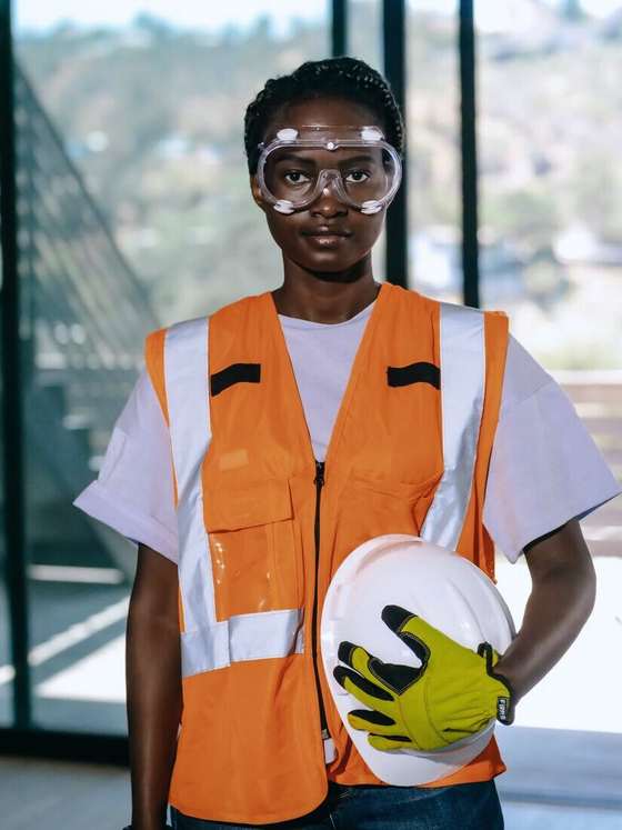 Operaria con chaleco naranja, lentes de seguridad y casco bajo el brazo