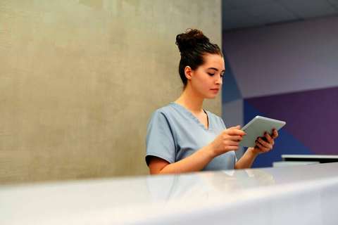 Recepcionista de una clínica mirando una tablet detrás del mostrador