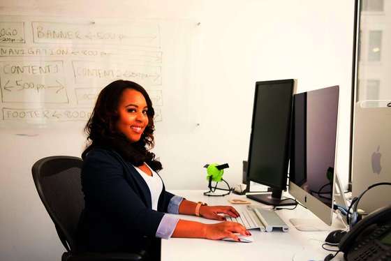 Mujer sonriendo sentada frente a una computadora en un escritorio de oficina