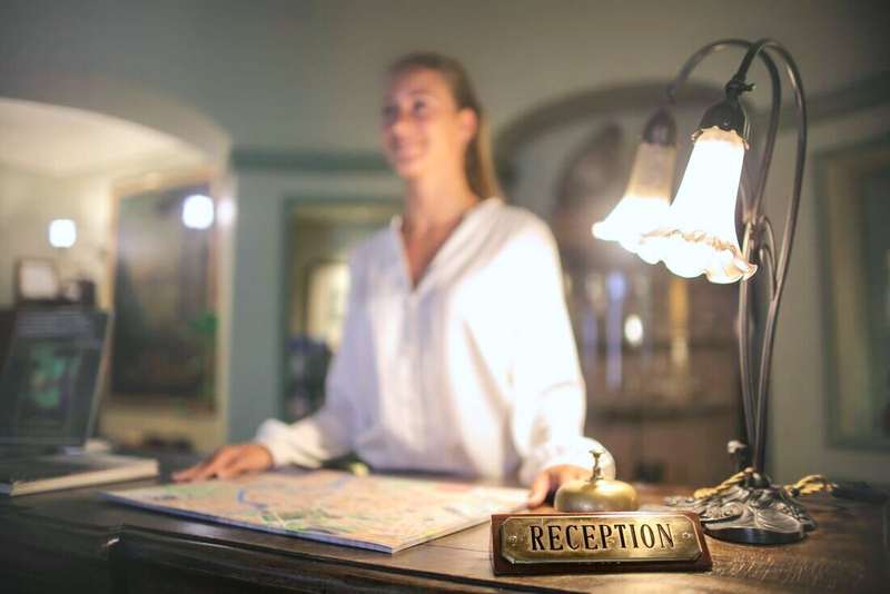 Recepcionista de hotel con blusa blanca junto a una lámpara sobre el mostrador