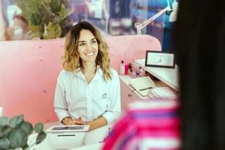 Recepcionista sonriendo detrás del mostrador mientras atiende a una persona
