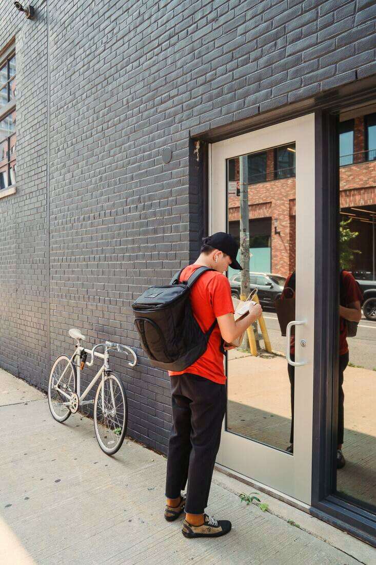 Repartidor con mochila junto a su bicicleta frente a una puerta de vidrio