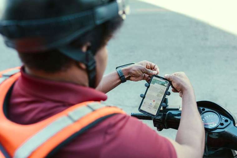 Repartidor con casco mirando el mapa en el celular fijado a su moto