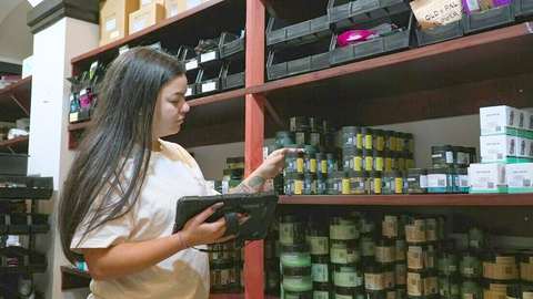 Mujer controlando mercadería con una tablet junto a un estante