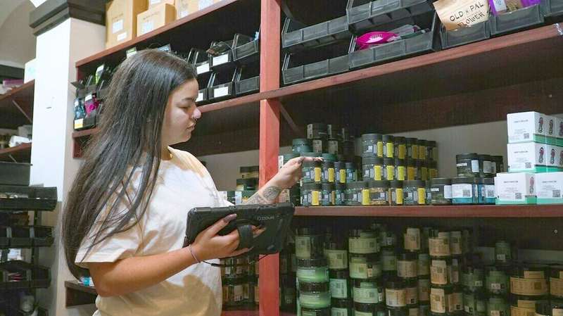 Mujer controlando mercadería con una tablet junto a un estante