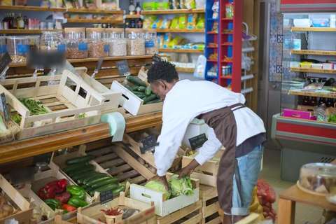 Empleado con delantal acomodando verduras en los cajones de una verdulería