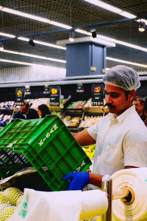 Empleado con cofia acomodando verduras en un supermercado