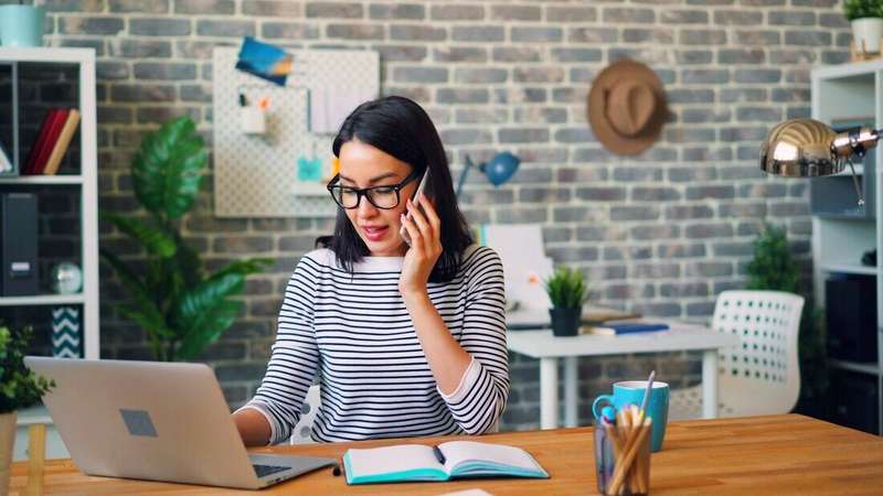 Mujer con anteojos hablando por celular frente a su notebook