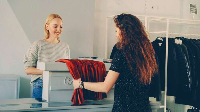 Vendedora mostrando una prenda a una clienta en el mostrador