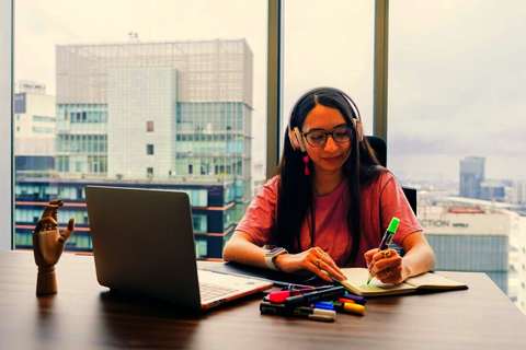 Mujer con auriculares anotando en un cuaderno junto a su notebook