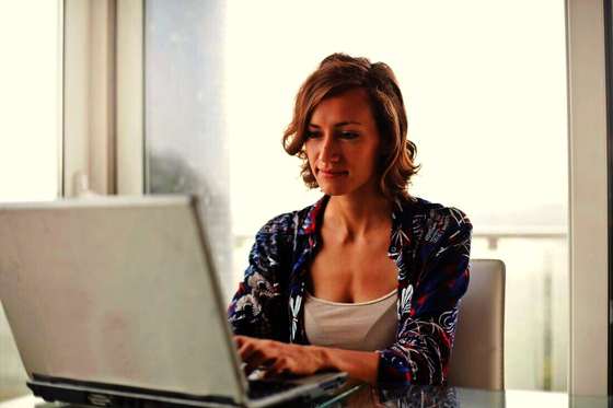 Mujer escribiendo en una notebook junto a una ventana