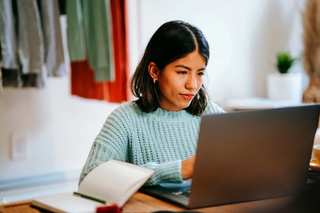 Mujer joven escribiendo en una notebook con un cuaderno al lado