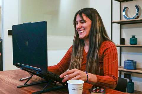 Mujer sonriendo frente a una notebook en un escritorio de madera